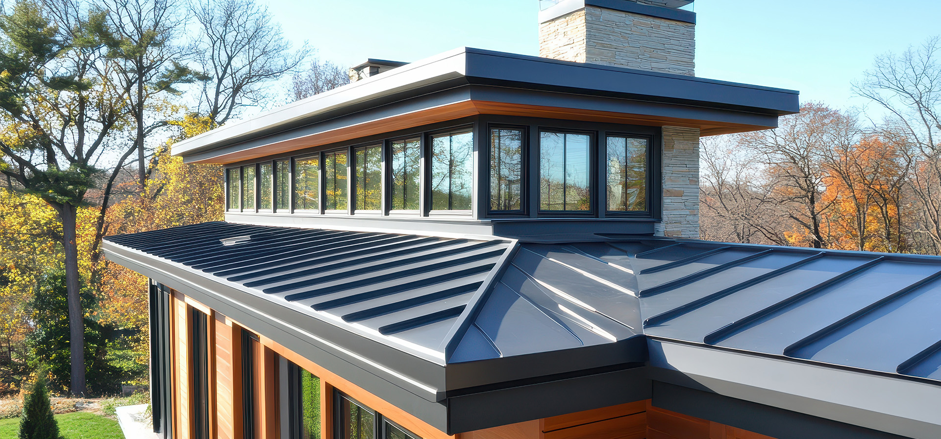 The image shows a modern residential building with an extended roofline featuring a prominent flat roof section, solar panels, and a combination of dark shingles and metal roofing.