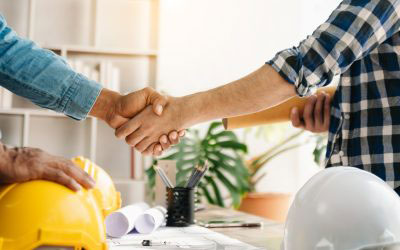 A group of three individuals shaking hands over a table with construction-related items, suggesting a professional agreement or partnership.